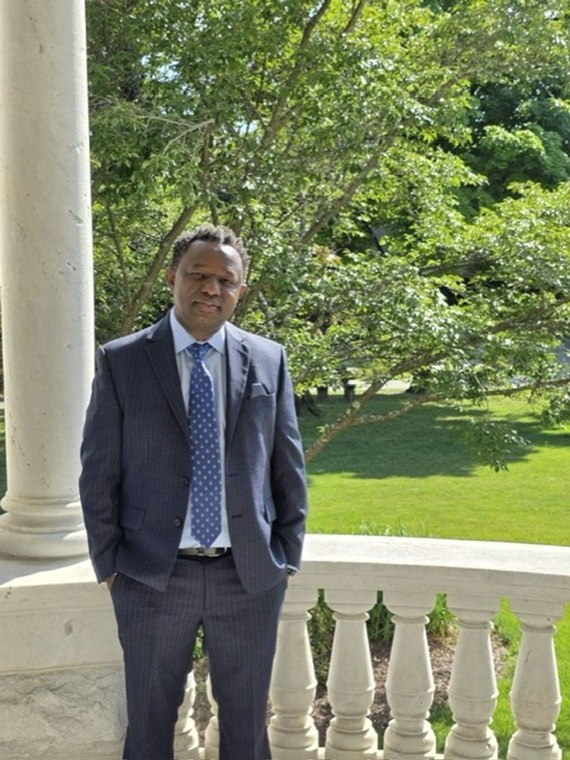 Charles Kangethe Charles Kangethe, candidate for Wawayanda Town Supervisor, standing on a porch in a dark suit and blue tie